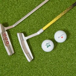 Two golf putters and two golf balls on grass.