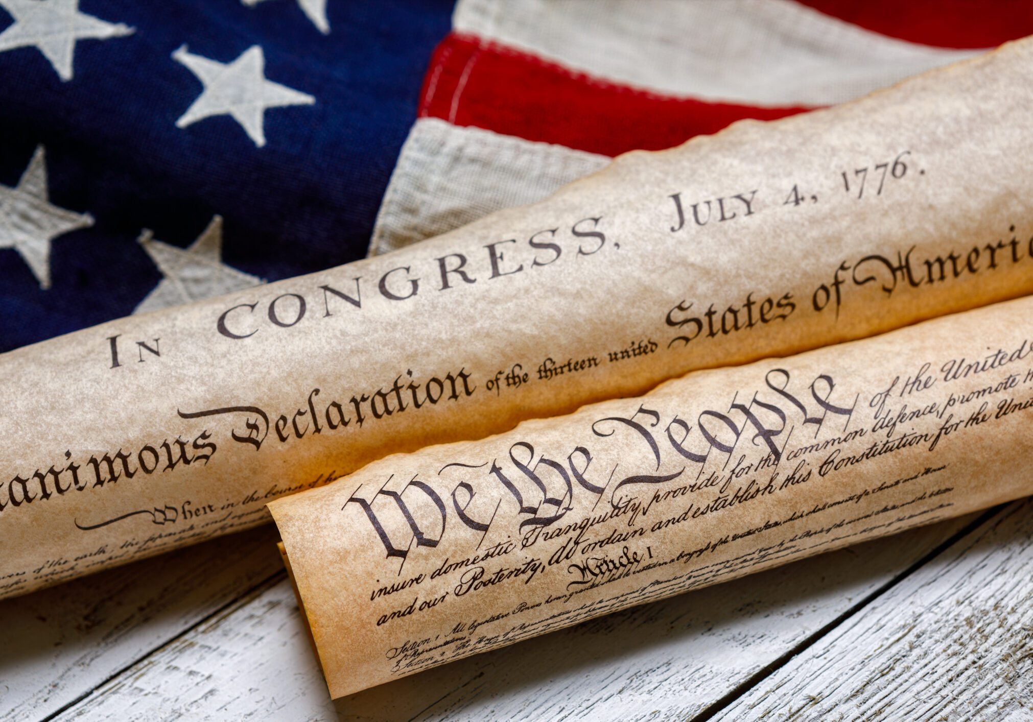 Rolled up copies of the US Constitution and Declaration of Independence with a vintage American flag on white painted weathered wood